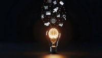Glowing lightbulb with business icons floating above on dark background representing innovation, creativity and entrepreneurial ideas for startup success.