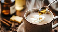 Honey dripping from spoon into creamy coffee drink with cinnamon sticks and spices on rustic wooden table, warm moody lighting creates cozy atmosphere.