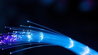 Fiber optic cables with glowing blue light streams and data particles flowing through high-speed internet connection on dark background for technology concepts.