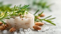 Homemade natural soap bar with fresh rosemary herbs and almonds on white wooden background with sea salt crystals for spa and skincare routine.