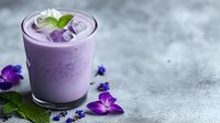 Refreshing purple smoothie with ice cubes, mint leaves and edible flowers on concrete background. Vibrant summer beverage with natural ingredients.