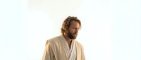 Middle-aged Caucasian man with beard in cream robe looking contemplative against soft light background for wellness and meditation content.