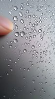 Raindrops on glass window create natural pattern with finger touching surface, soft gray background with water condensation droplets showing surface tension.