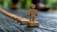 Wooden figure standing on domino pieces arranged in line on rustic wooden surface, representing leadership, risk, and business decision concept.