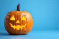 Glowing carved pumpkin with classic jack o'lantern face featuring triangular eyes and jagged smile on vibrant blue background with copy space for seasonal designs.