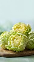 Fresh green iceberg lettuce heads on wooden cutting board ready for healthy salad preparation and cooking in bright kitchen setting.