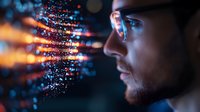 Young male professional in profile view examining glowing data visualization with streaming digital code particles in dark environment with blue and orange light effects.