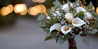 White calla lilies and roses wedding bouquet with eucalyptus and baby's breath against blurred golden bokeh lights, romantic floral arrangement.