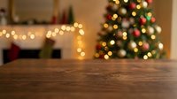 Empty wooden table surface with blurred Christmas tree and warm lights in cozy living room background for holiday product display and festive decorations.