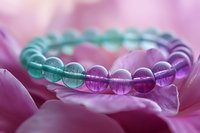 Colorful gradient healing crystal bracelet with turquoise and purple beads resting on pink flower petals, showcasing spiritual wellness and meditation accessories.