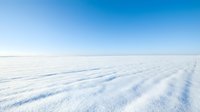 Vast frozen lake or snow-covered landscape with rippled surface patterns under clear blue sky, suitable for winter backgrounds and nature projects.