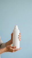 Male hand holding blank white spray bottle against light blue background for product mockup and branding purposes.