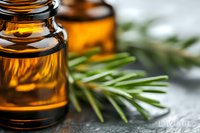 Essential oil amber glass bottle with fresh rosemary sprig on stone surface, selective focus macro shot showing aromatherapy and natural wellness concept.