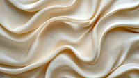 Luxurious cream-colored silk fabric with elegant waves and soft folds creating smooth flowing curves and gentle shadows on textured satin material background.