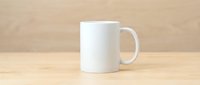 White ceramic coffee mug mockup on a wooden table with a light wood background, blank surface ready for custom design or logo.