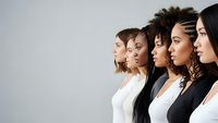 Diverse group of women standing in profile showing multicultural beauty and unity in professional business attire against neutral background.