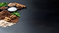 Baking ingredients cocoa powder flour walnuts cinnamon sticks mint leaves arranged on dark slate background with copy space for culinary recipes and cooking.
