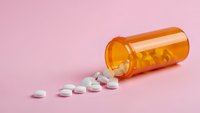 Orange prescription pill bottle spilled white tablets on pink background healthcare medication concept for medical design projects.