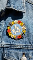 Floral enamel pin with be kind lettering on blue background, decorated with wildflowers, pinned on denim jacket. Kindness accessory concept.