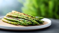 Fresh green asparagus spears arranged on white ceramic plate against dark background with soft natural lighting, showcasing seasonal vegetable for food photography.
