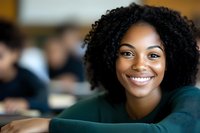 Young African American woman with natural curly hair and bright smile wearing green sweater in office or educational setting, looking directly at camera with confident expression.