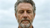 Middle-aged man with gray hair and beard, caucasian ethnicity, displaying a calm, contemplative expression with eyes closed against a soft, overcast sky background.