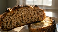 Freshly baked artisan sourdough bread loaf with crusty exterior and open crumb structure, sliced and displayed in natural sunlight for bakery, food photography, and culinary content.