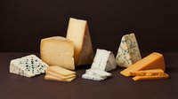 Assorted gourmet cheese selection with blue cheese, aged cheddar, brie and hard cheeses arranged on dark background for culinary photography.