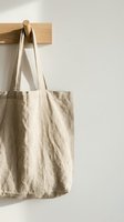 Natural linen tote bag hanging on wooden peg against white wall. Eco-friendly reusable shopping bag for sustainable lifestyle and zero waste living.