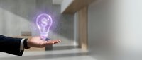 Businessman hand holding glowing purple lightbulb with dollar sign symbol representing innovative financial ideas and profitable business solutions in modern office.