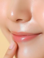 Close-up of Asian female face showing smooth glowing skin, natural pink lips, and finger touching lower lip against yellow background. Suitable for beauty and skincare ads.