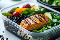 Grilled salmon with black beans, cherry tomatoes and fresh greens in glass meal prep container. Healthy lunch box ready for office or gym nutrition planning.