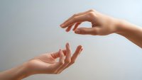 Two hands reaching toward each other in gentle gesture of connection, support and care against soft neutral background for wellness concepts.