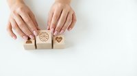 Woman's hands arranging wooden blocks with health, wellness and love symbols on white background. Concept for healthcare, medical insurance, wellbeing and lifestyle choices.