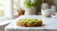Fresh avocado toast on rustic bread with herbs and seeds served on white plate in bright kitchen setting for healthy breakfast or brunch meal.