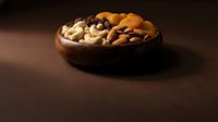 Mixed nuts and dried fruits in wooden bowl on dark surface for healthy snacking and gourmet food photography.