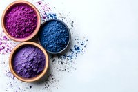 Vibrant purple and blue natural powder pigments in ceramic bowls on white background with scattered colorful dust, artistic composition for cosmetics and dyes.