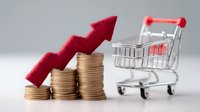 Rising stack of gold coins with red upward arrow and shopping cart on gray background, representing retail price inflation and consumer spending growth.