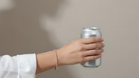 Hand holding aluminum beverage can with silver bracelet against neutral background for refreshment and drink advertising concepts.