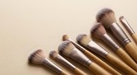Professional makeup brushes with golden handles arranged on neutral beige background for cosmetic application and beauty routine essentials.