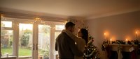 Man decorating Christmas tree at home during golden hour with warm lighting and festive holiday atmosphere in cozy living room setting.