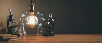 Vintage laboratory workspace with glowing Edison bulb, antique microscopes and scientific equipment on wooden desk creating atmospheric research environment.
