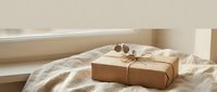 Kraft paper gift box with natural twine and eucalyptus leaves on linen fabric by window. Minimalist eco-friendly packaging for holidays and special occasions.