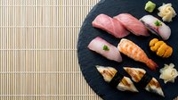Assorted nigiri sushi and sashimi arranged on black slate plate with bamboo placemat, featuring raw fish, seafood, and rice preparations for Japanese cuisine dining and restaurant menus.
