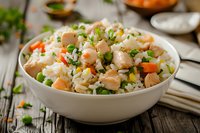 Fresh seafood rice bowl with tender shrimp, diced carrots, green peas, and chopped herbs served in white ceramic dish on rustic wooden table, food photography.