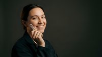 Happy businesswoman talking on smartphone with warm smile against dark background for corporate communication and professional networking.