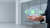 Businessman holding holographic green battery icon with charging symbol floating above palm in modern office environment for renewable energy concepts.