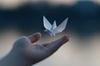 Delicate origami butterfly hovering above an outstretched palm against soft bokeh background, symbolizing freedom, hope and transformation in minimalist style.