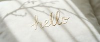 Embroidered hello lettering on soft linen fabric with delicate branch shadows, cozy minimalist textile background for greeting cards and home decor.