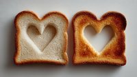 Two slices of toast with heart-shaped cutouts showing different toasting levels, one lightly golden and one darker brown, arranged side by side on white surface.